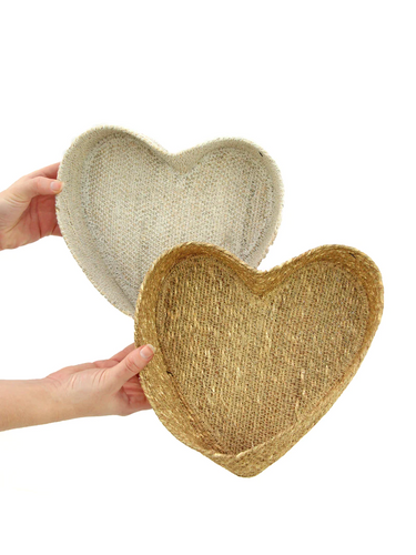 Two hands holding, each holding a heart shaped basket. One basket, in the front, is a natural color. The basket in the back is white.